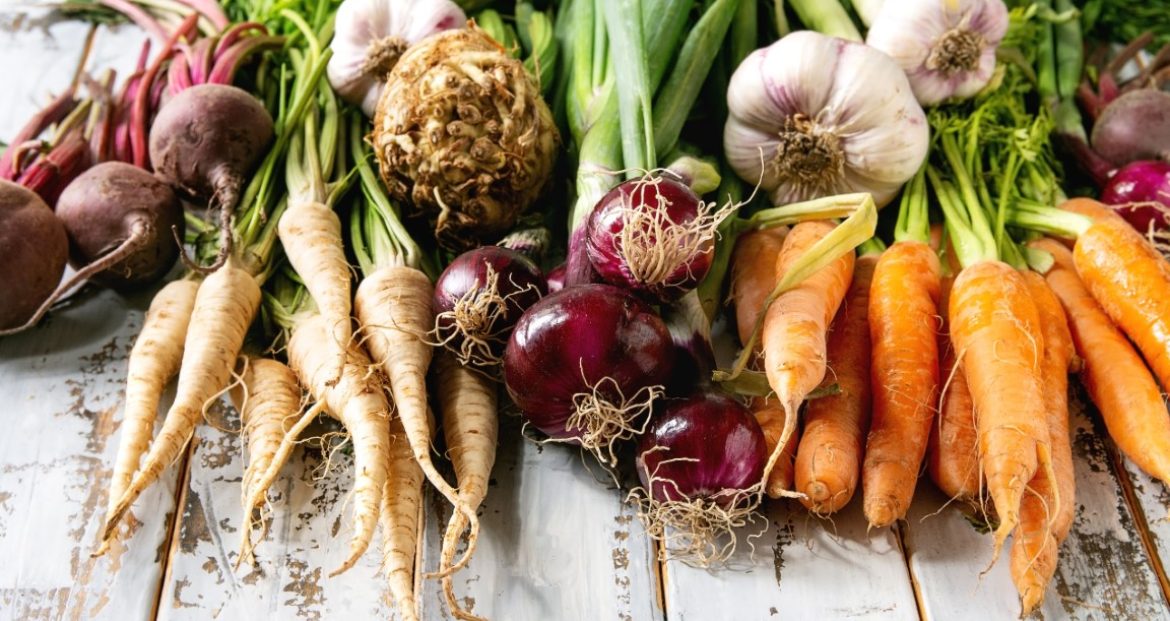 Variety of root garden vegetables carrot, garlic, purple onion, beetroot, parsnip and celery with tops over white wooden background. Flat lay, space